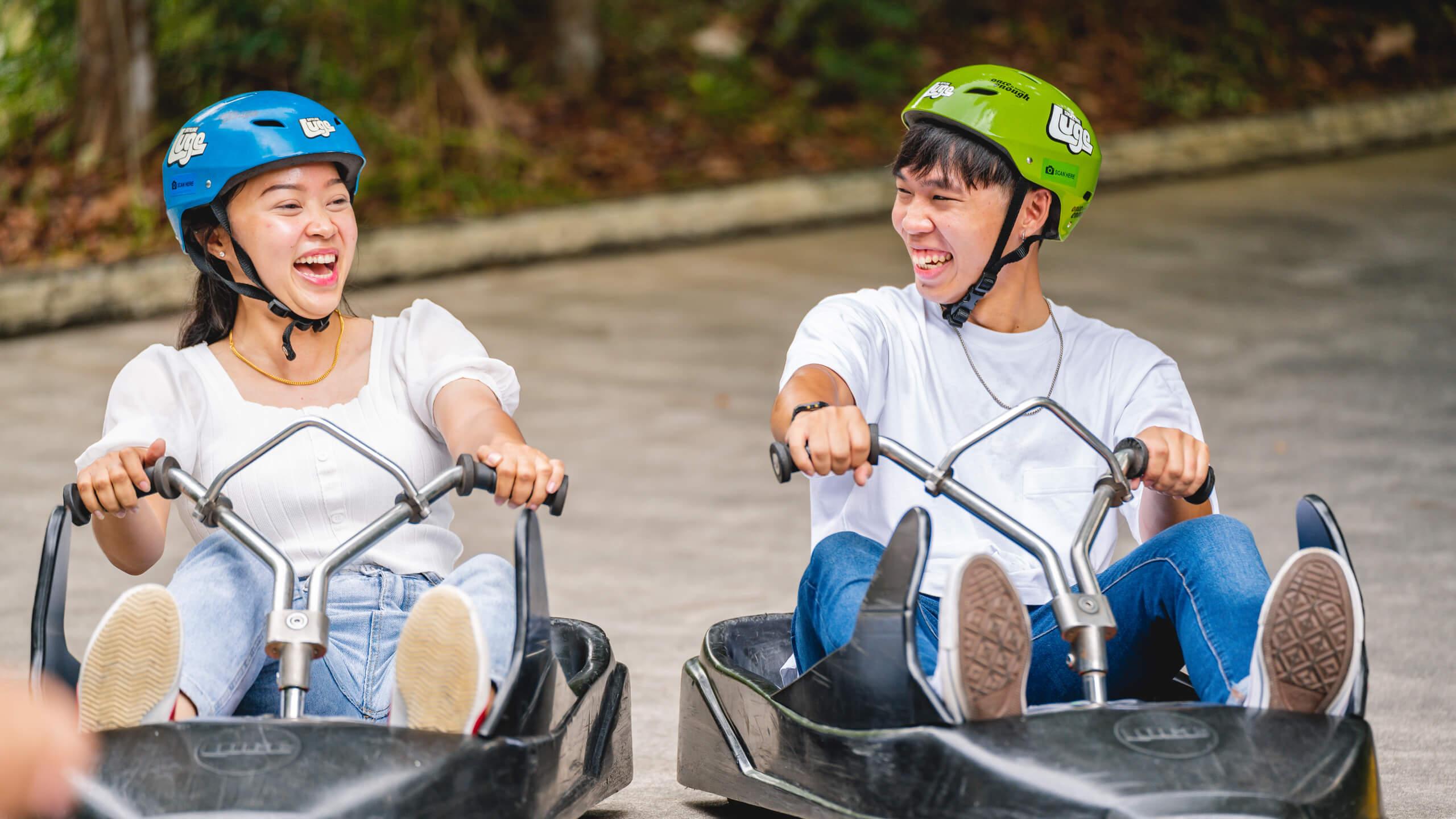 Two friends smile and giggle as they ride next to each other on the Luge tracks.