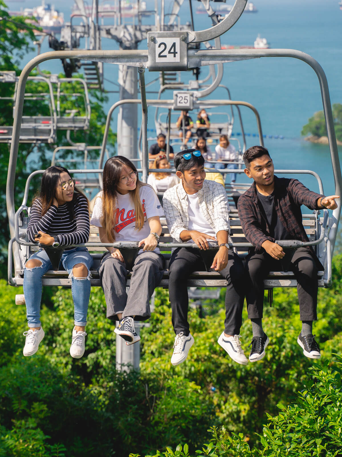 A group of friends point and look at something whilst riding the Skyride chairlift at Skyline Luge Singapore.