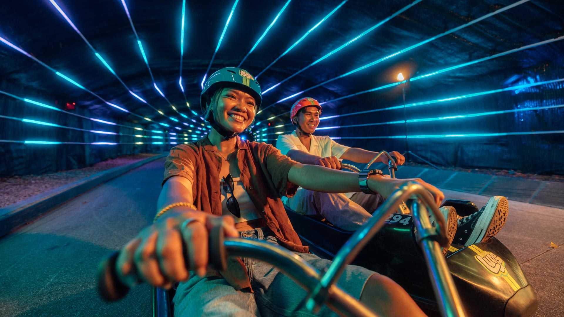 Skyline Luge a Pair of Youths enjoying Neon Lit Tunnels in Night Luge